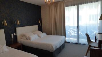 Una habitación de hotel con una cama grande, dos mesitas de noche con lámparas, un escritorio con silla y un ventanal con cortinas.