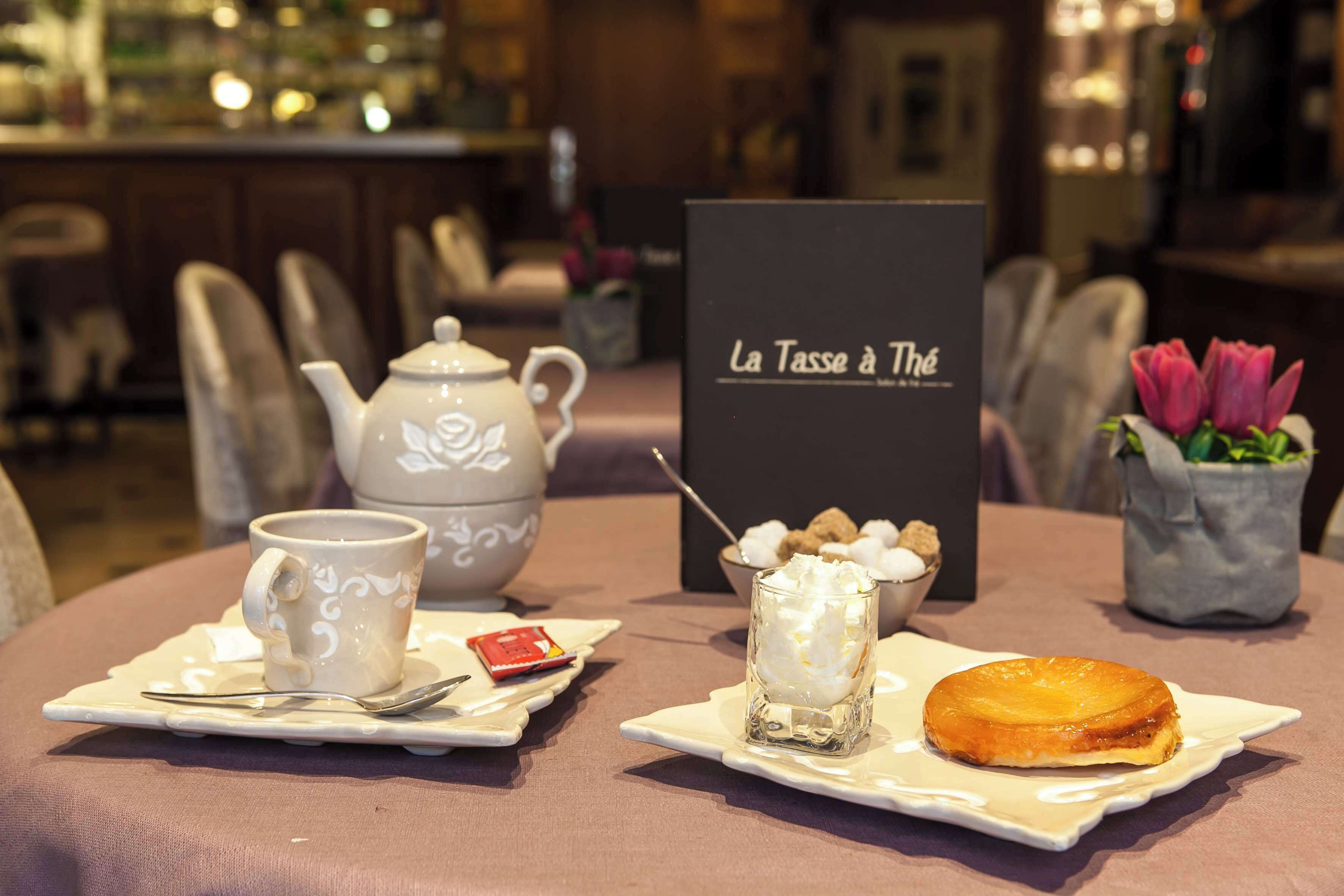 A table set with a teapot, a cup, a glass of whipped cream, a dessert, and a sign reading "La Tasse à Thé".