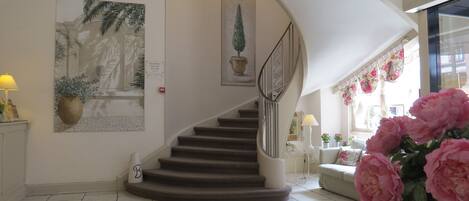 Un escalier avec une rampe, un pot de fleurs et un panneau fixé au mur.