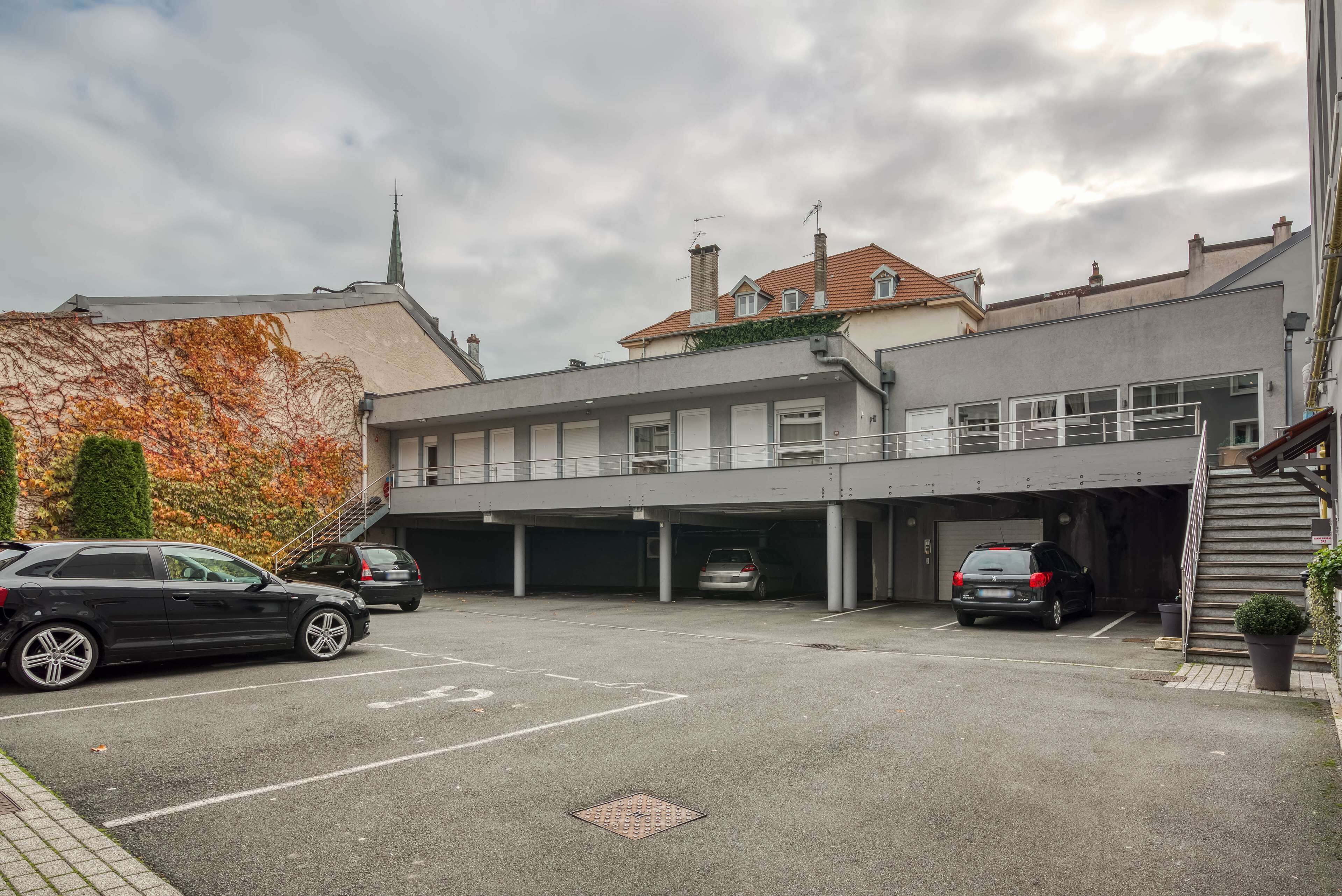 A parking area with several cars, a building with a flat roof, and a church steeple in the background.