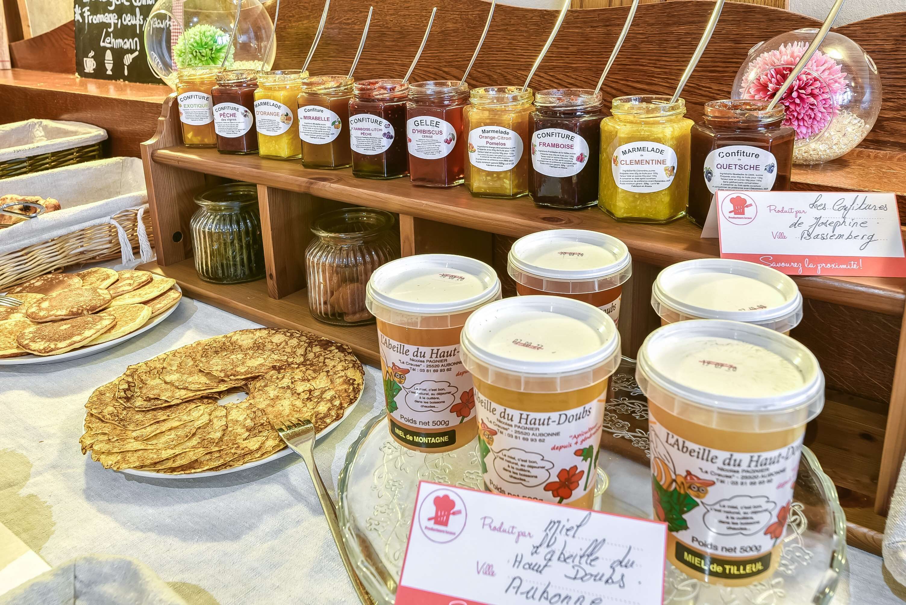 Een presentatie van diverse etenswaren, waaronder potten jam, een schaal pannenkoeken en bakjes honing.