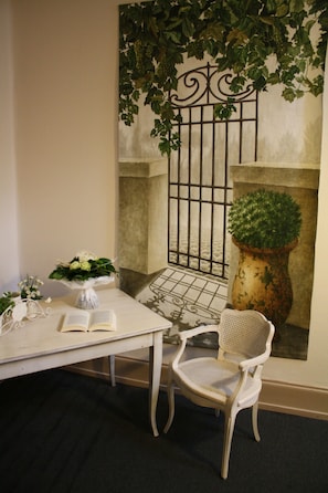 Een kamer met een witte tafel, een stoel, een potplant en een decoratieve wand met een poort en groen.