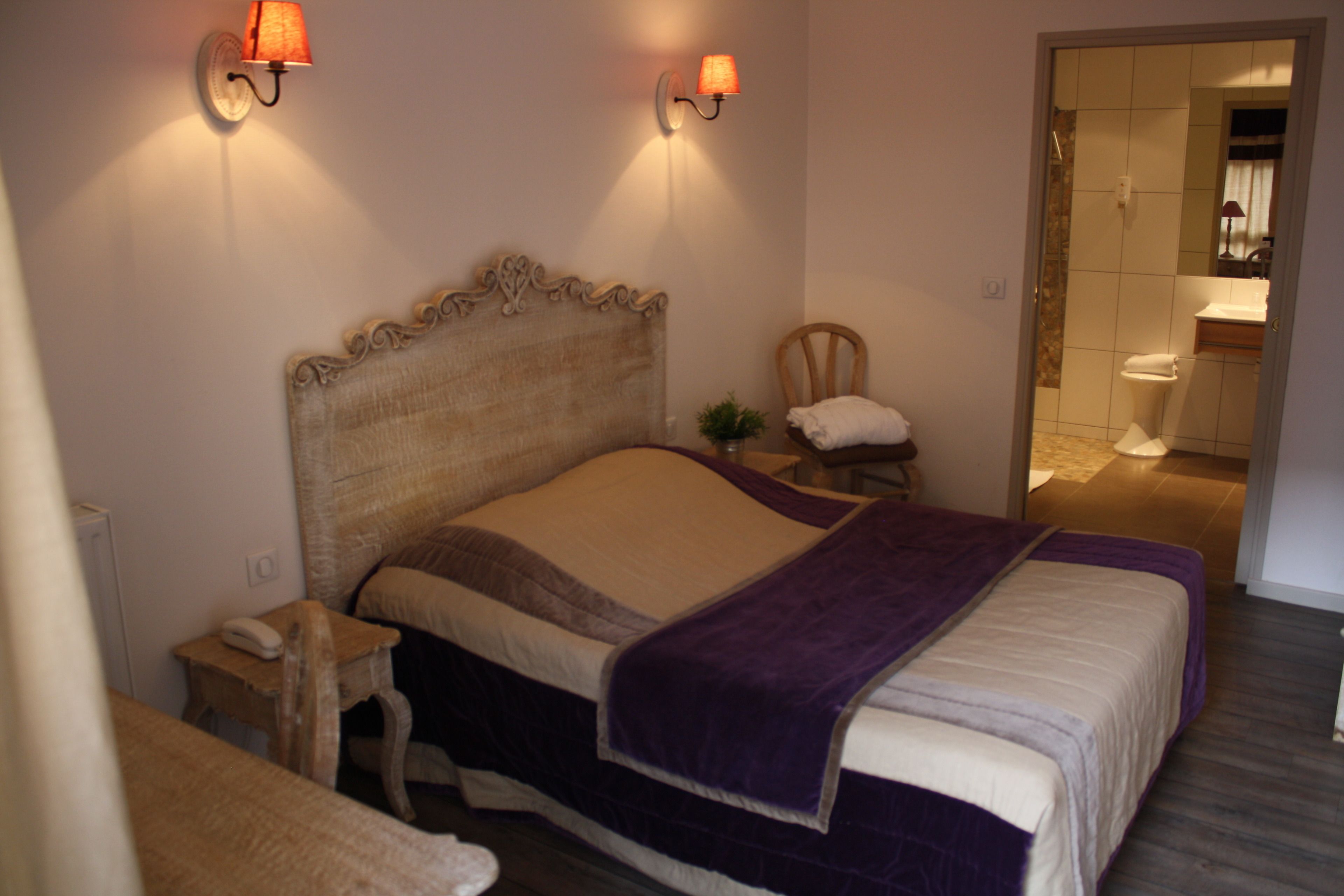 A bedroom with a large bed, bedside tables, a chair, and a bathroom visible through an open door.