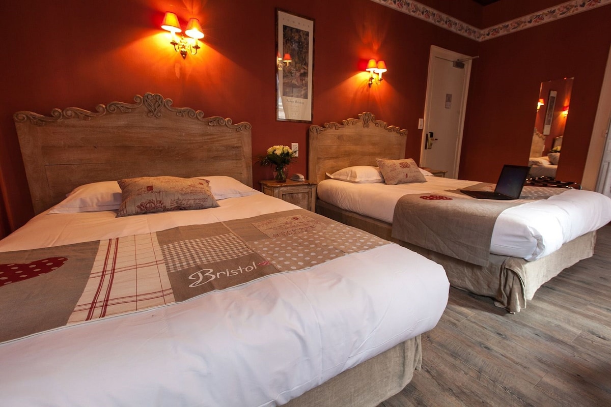 Een hotelkamer met twee bedden, elk voorzien van een houten hoofdeinde, witte beddengoed, en een laptop op een van de bedden.