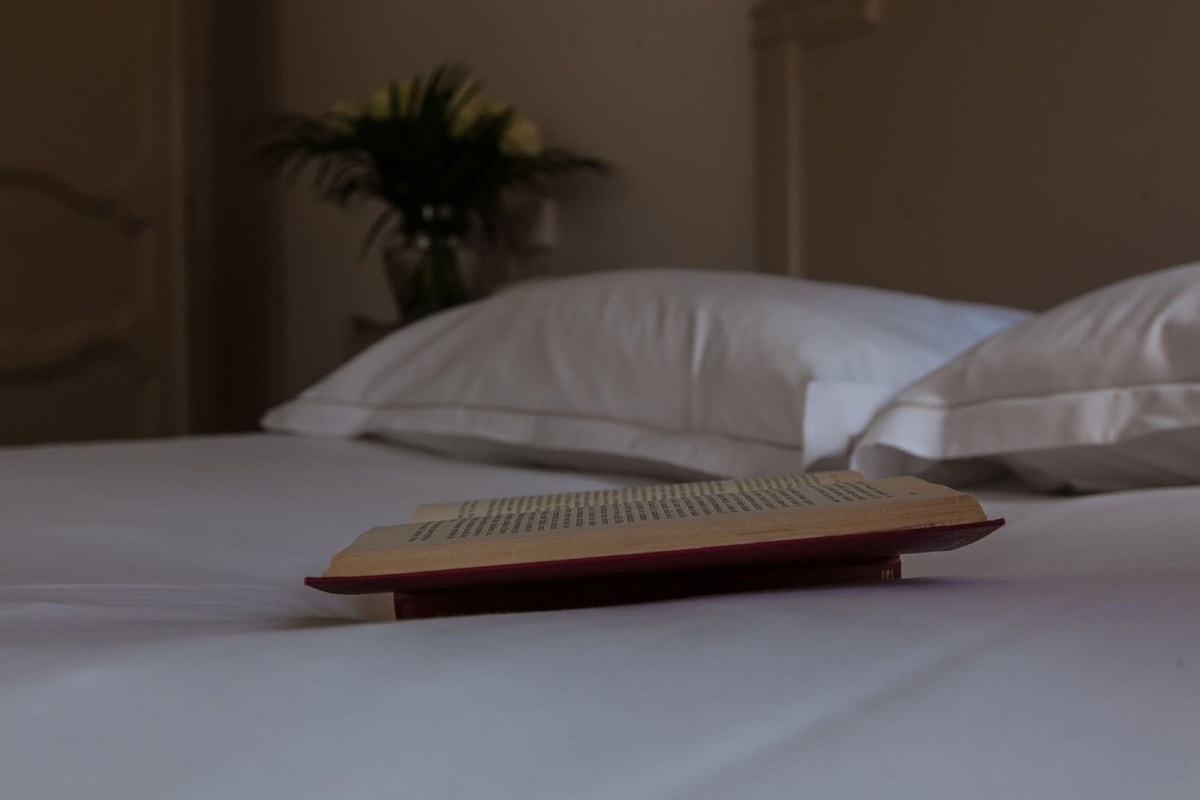 Een bed met witte lakens en een boek erop.