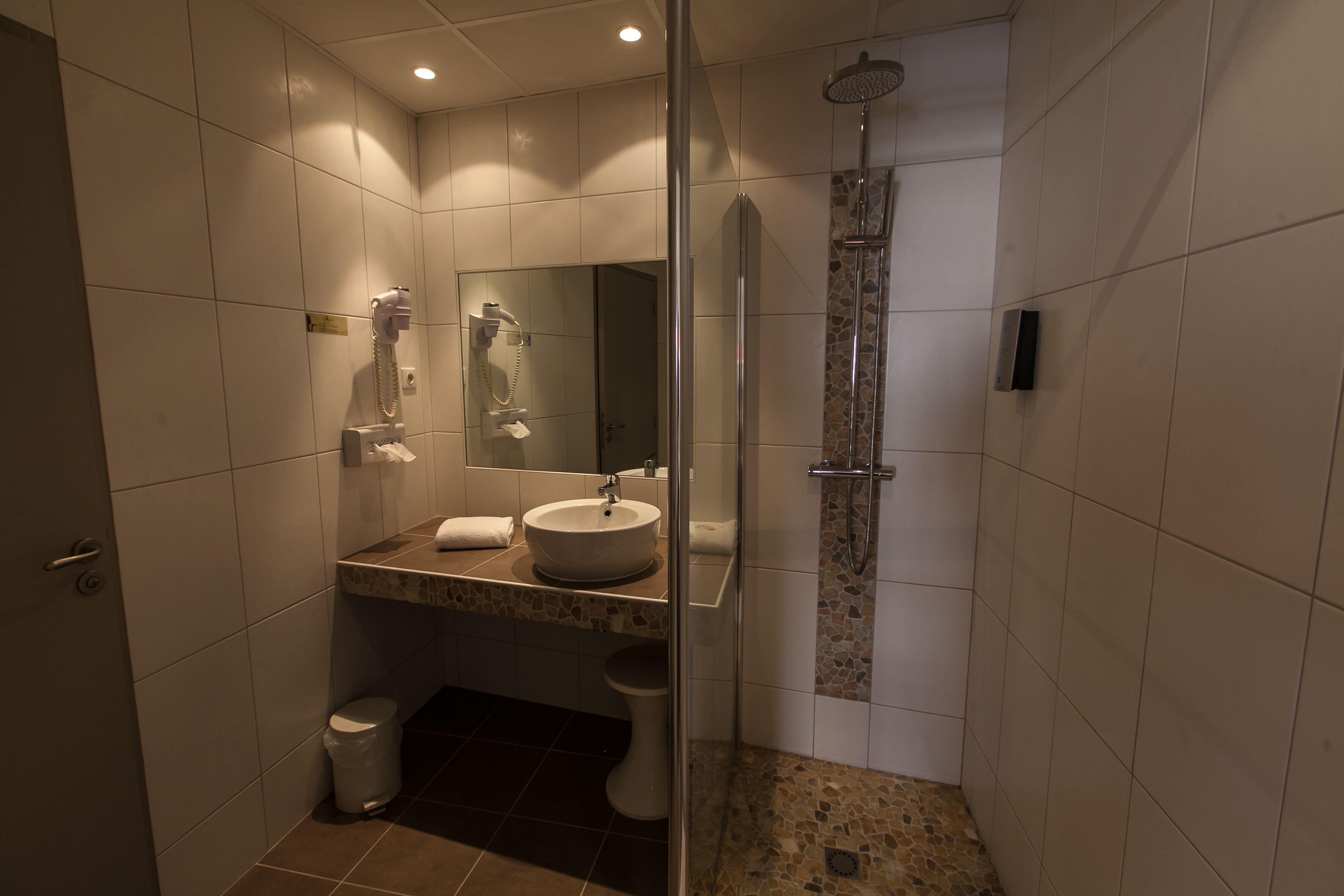 Un baño moderno con ducha de vidrio, lavamanos con espejo y retrete.