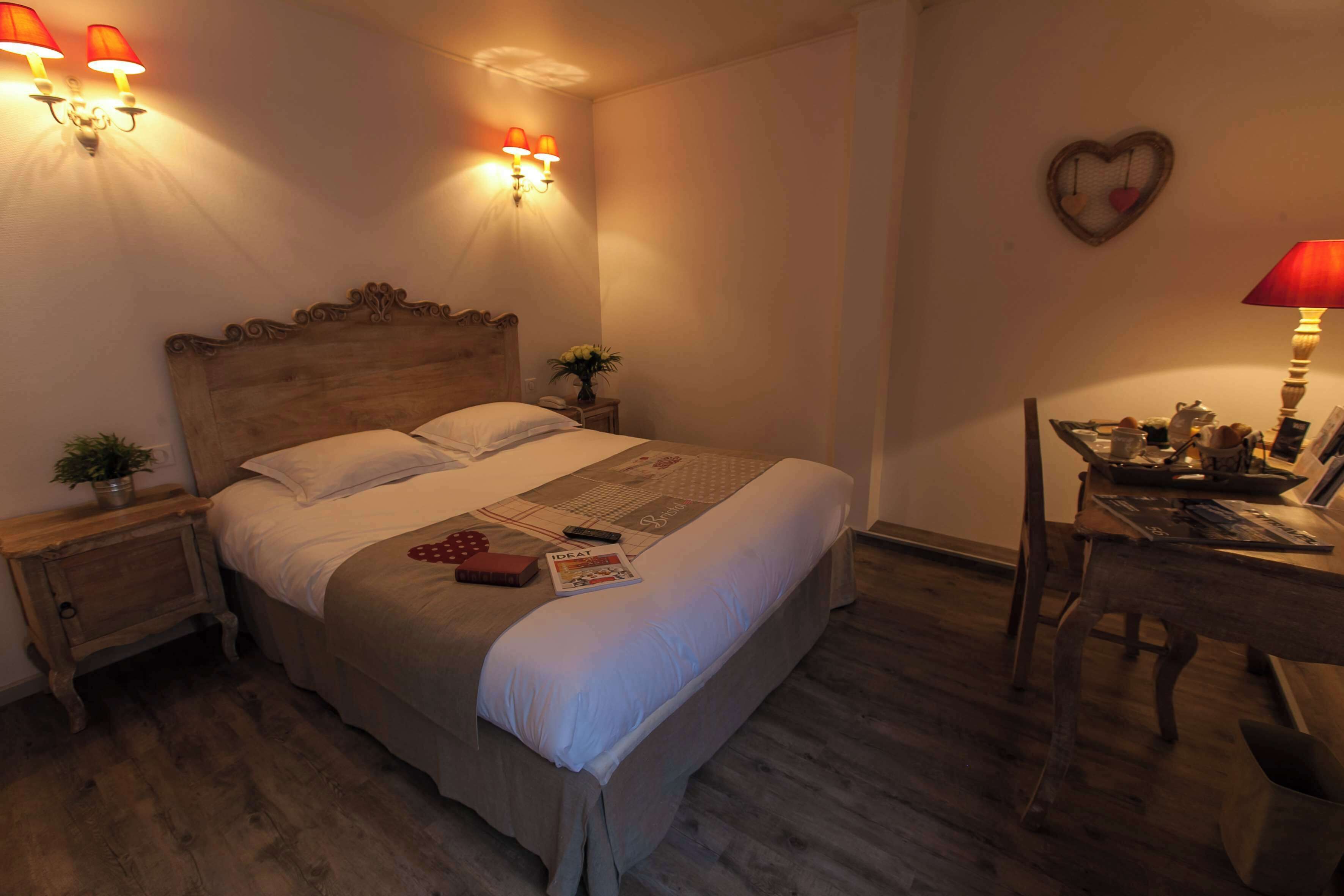 Een slaapkamer met een houten bed, twee nachtkastjes, een bureau met stoel, en wandlampen.