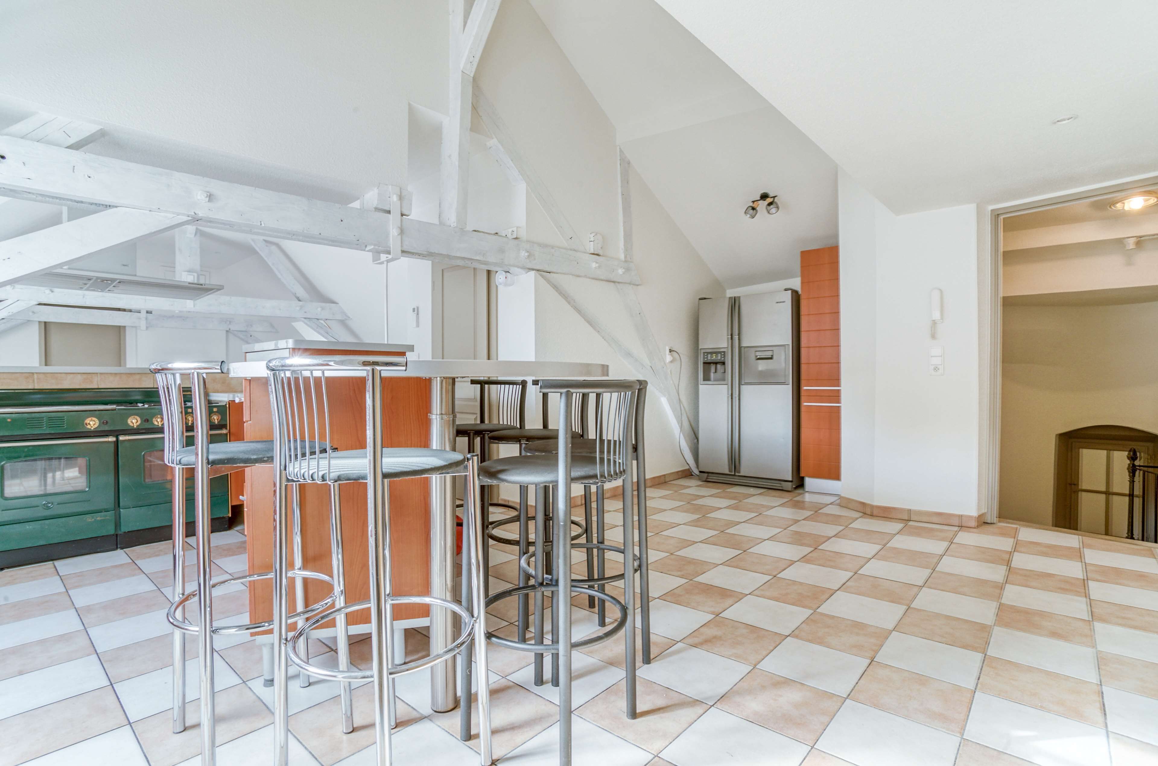 A spacious kitchen with high ceilings, a dining area with metal bar stools, and a checkered floor.