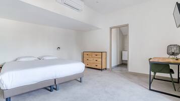 A modern bedroom with a bed, a wooden dresser, a desk with a chair, and an air conditioning unit.