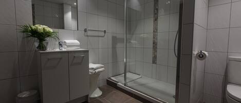 A modern bathroom with a glass-enclosed shower, a toilet, and a vanity with a mirror and a vase of flowers.