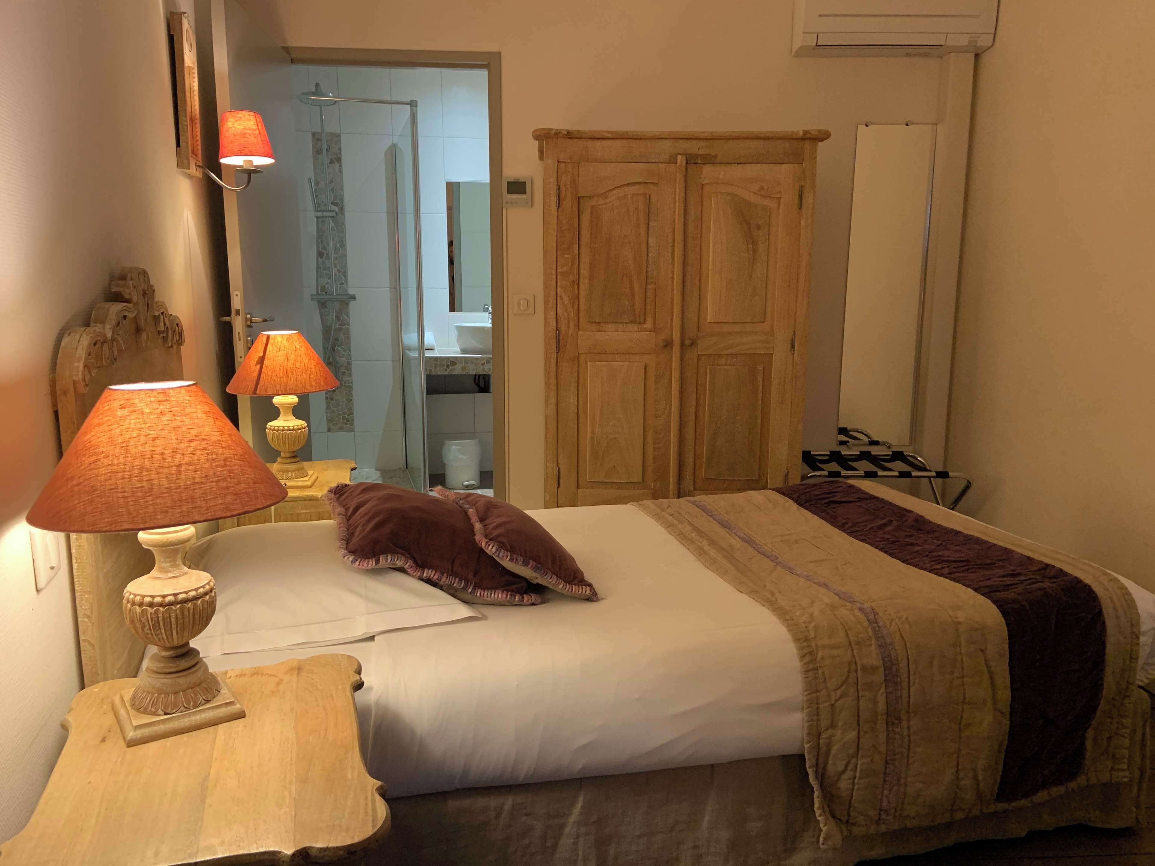 A bedroom with a bed, two bedside lamps, a wooden wardrobe, and a mirror.