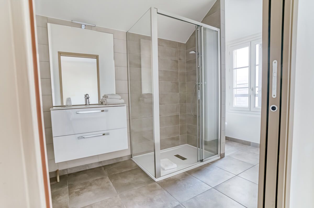 A modern bathroom with a glass-enclosed shower, a white vanity with a mirror, and a tiled floor.