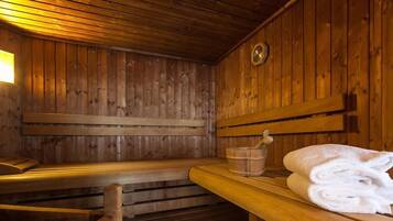 Una sauna de madera con bancos, un cubo de madera y una toalla doblada sobre un banco.