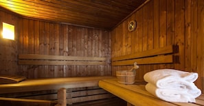 Een houten sauna met banken, een houten emmer en een opgevouwen handdoek op een bank.