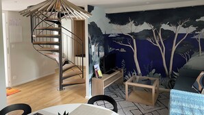 Una sala de estar moderna con una escalera espiral, un mural de árboles y una mesa de centro de vidrio.