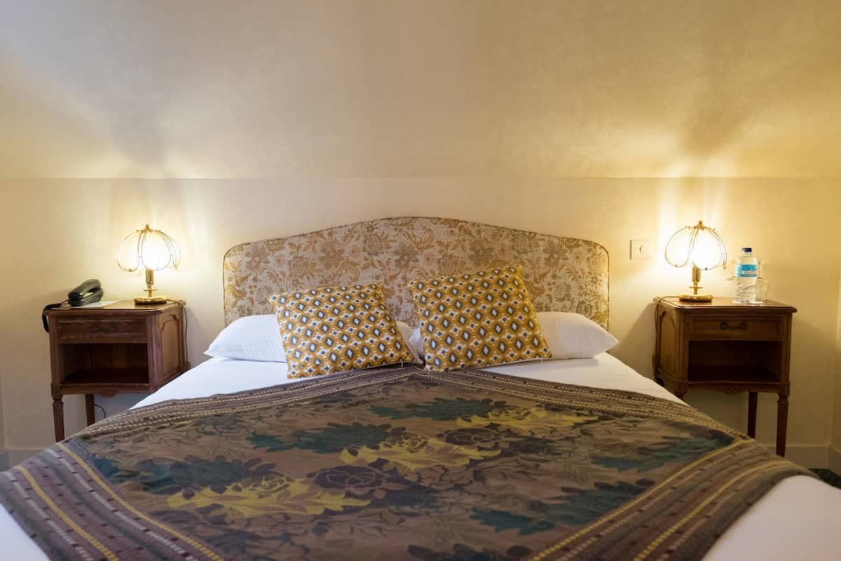 Habitación de hotel con una cama grande, dos mesitas de noche con lámparas y un cabecero floral.