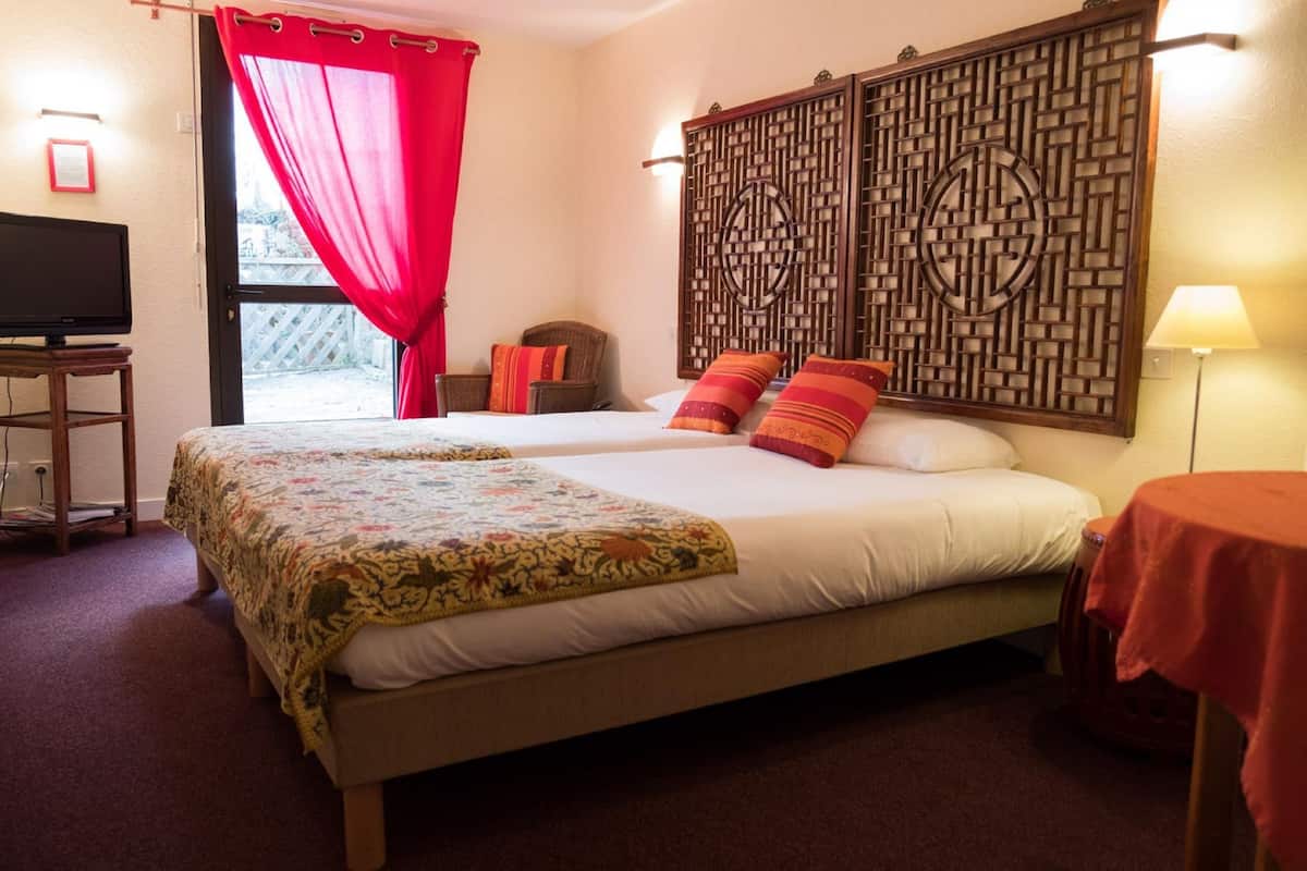 Habitación de hotel con dos camas, un televisor, una cortina roja y un panel decorativo en la pared.