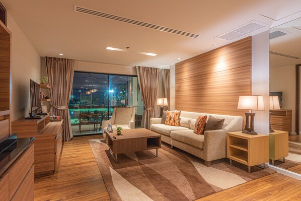 A modern living room with a sofa, coffee table, and lamps. There is a large window with curtains, a wooden accent wall, and a view of the city at night.
