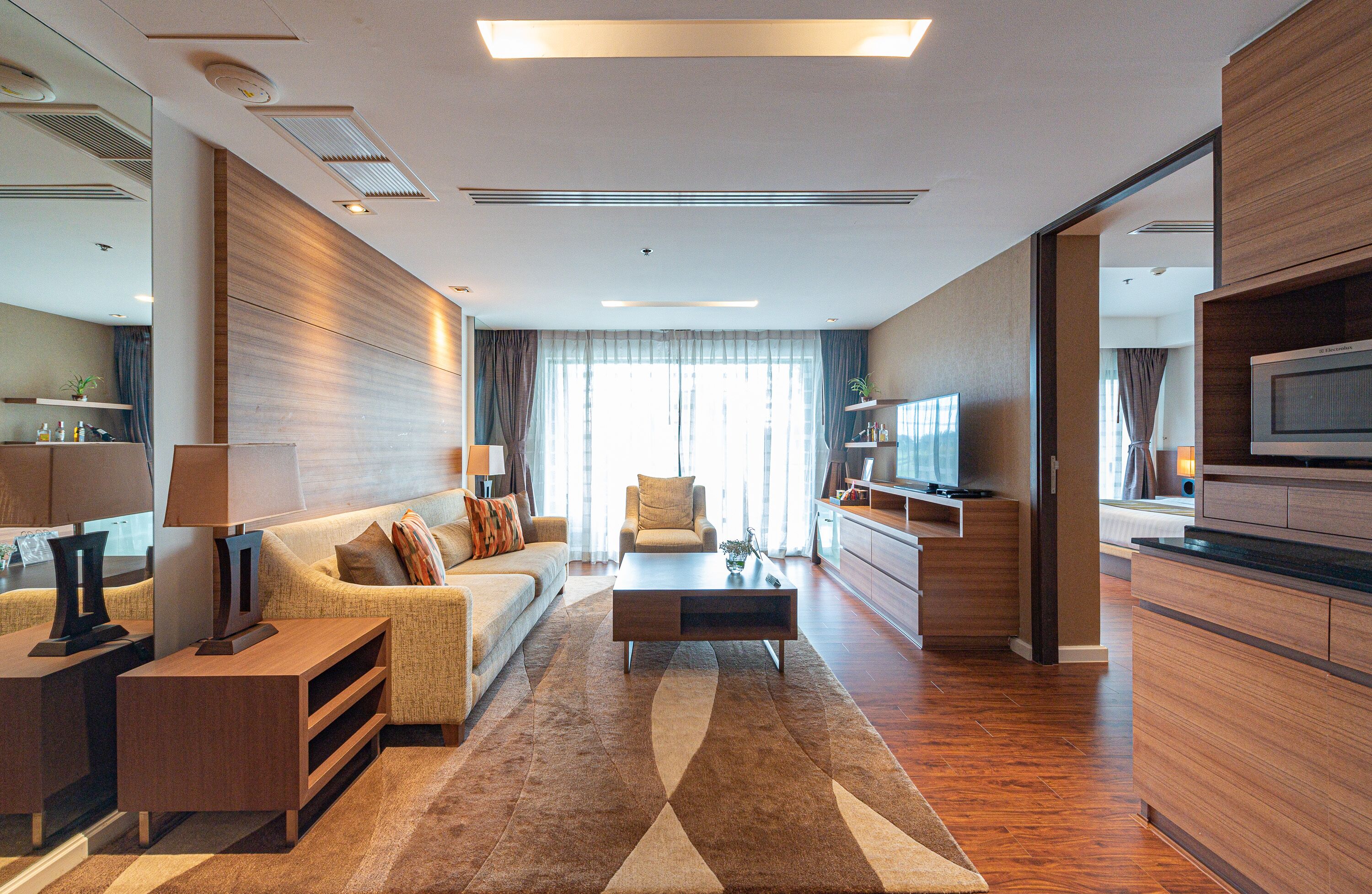 A modern living room with a sofa, coffee table, and TV. There is a kitchen area with a microwave and cabinets.