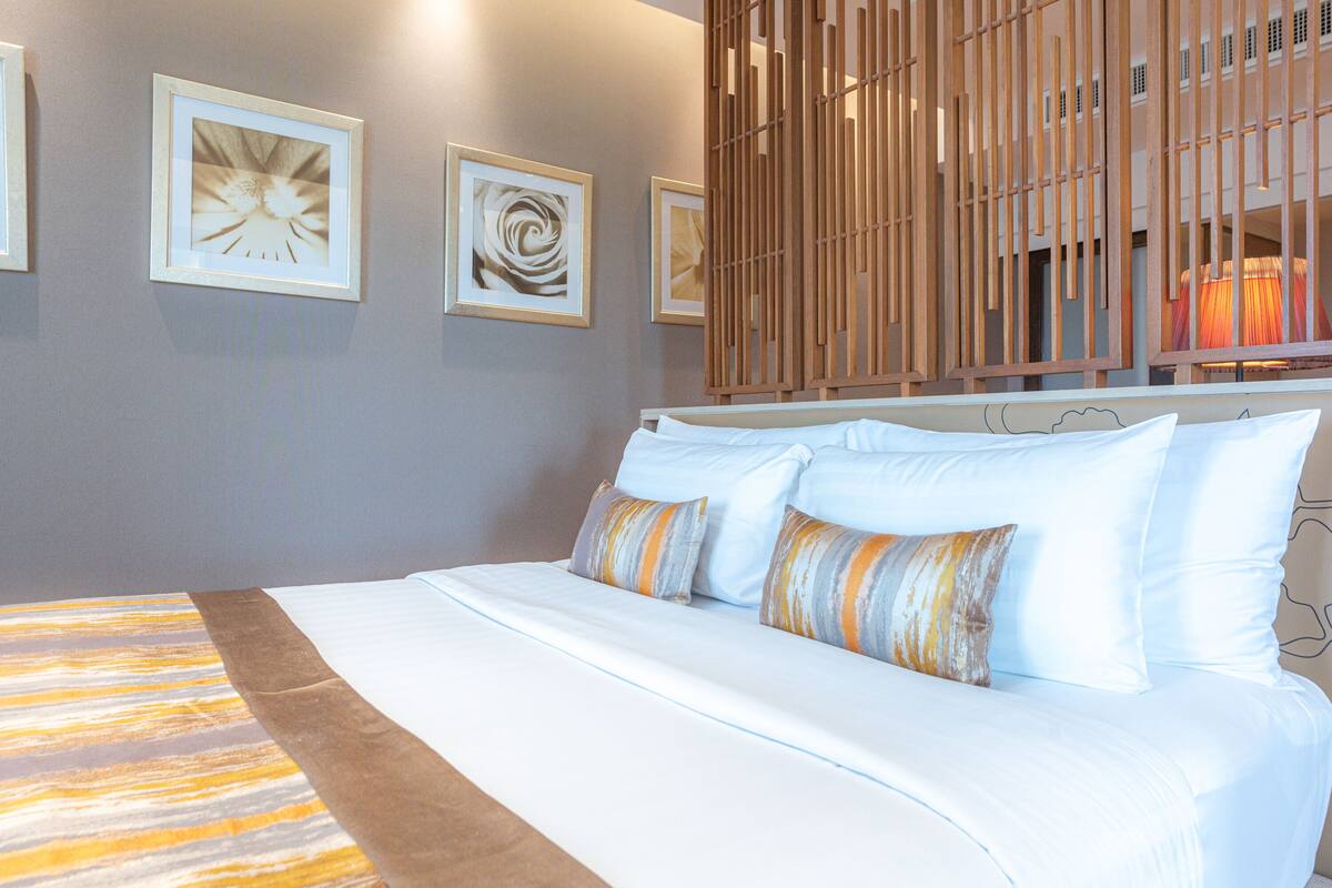 Una cama bien hecha con sábanas blancas y almohadas a rayas, un cabecero de listones de madera y cuadros en la pared.