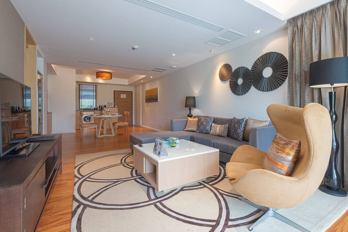 Una sala de estar moderna con un sofá, un sillón y una mesa de centro. En el fondo, hay una zona de comedor con una mesa y sillas.