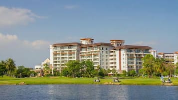 Enjoy expansive views from the hotel's large windows and balconies, overlooking a tranquil waterfront setting with lush greenery and palm trees.