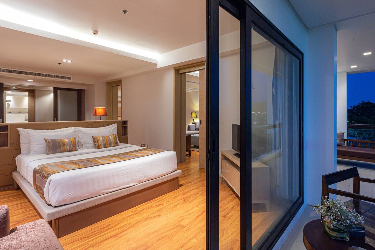 Una habitación de hotel moderna con una cama grande, un balcón con vistas y una zona de estar separada.