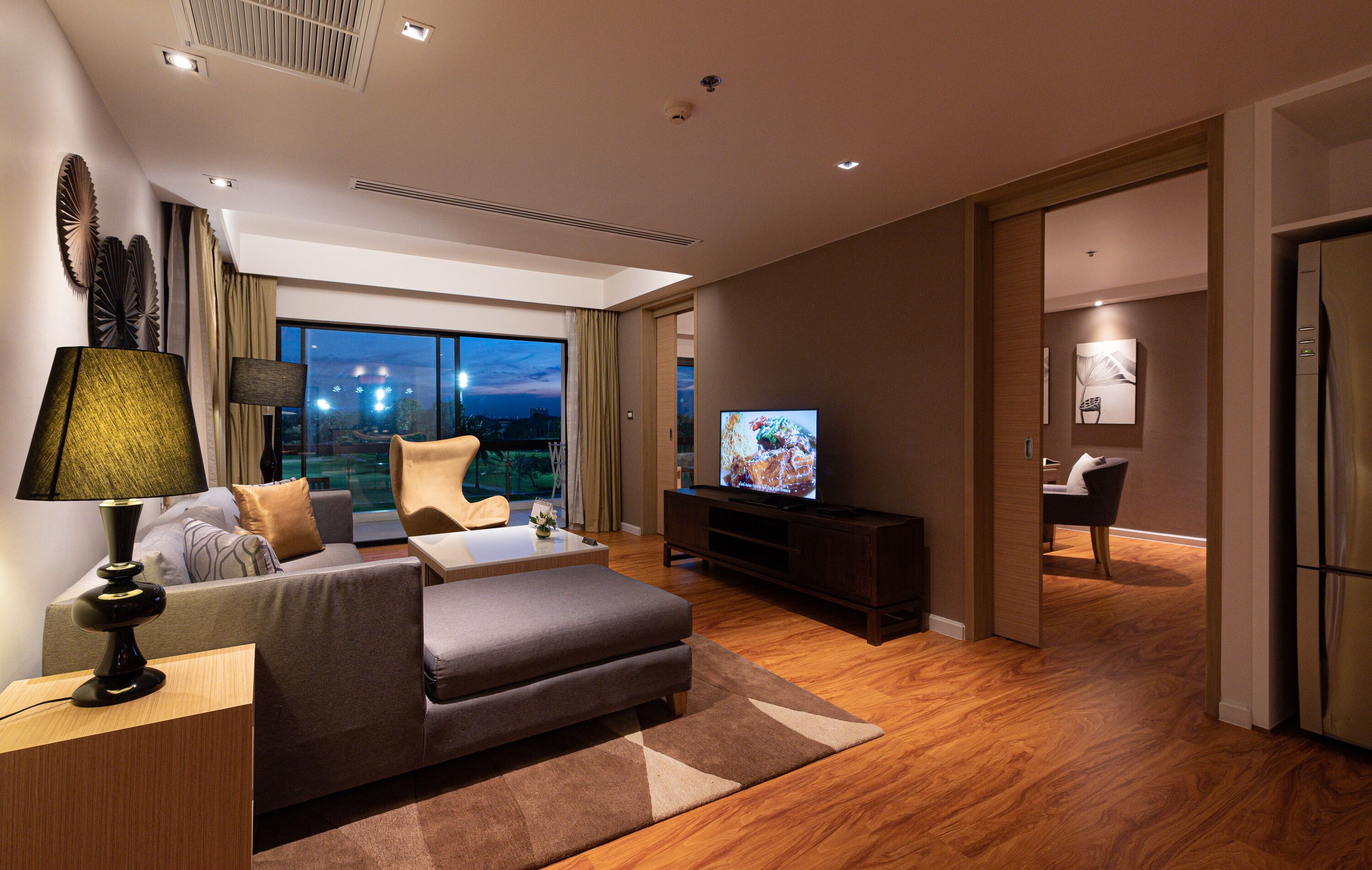 A modern hotel room with a sofa, TV, and a view of the city at night.