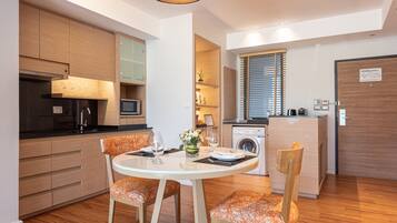 A modern kitchen with wooden cabinets, a dining table with orange chairs, and a built-in washing machine.
