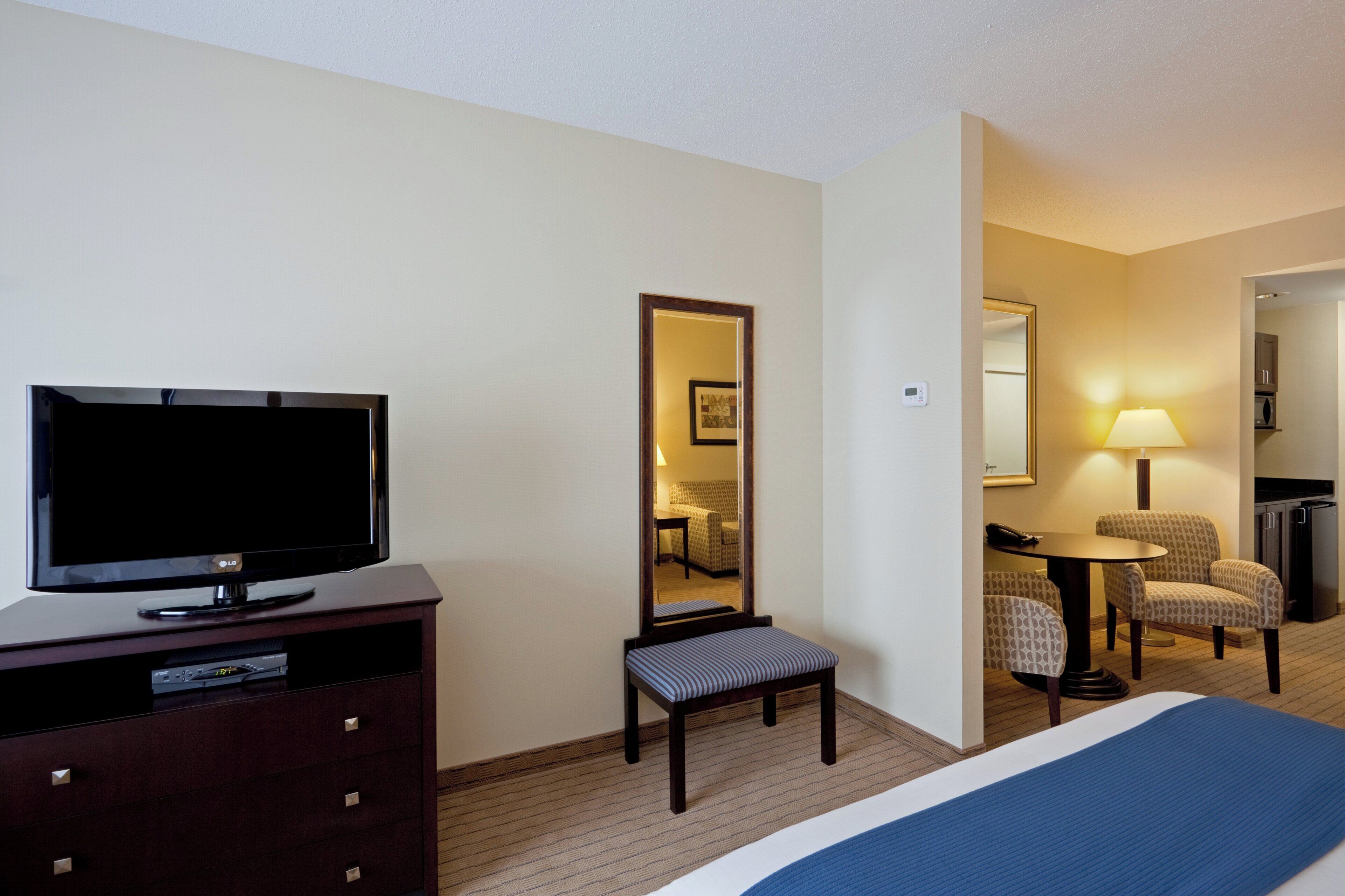 A hotel room with a bed, a television, a desk with a lamp, a chair, and a mirror.