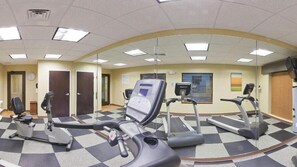 Une salle de sport équipée de tapis de course et de vélos elliptiques, avec un sol à carreaux et un mur recouvert de miroirs.