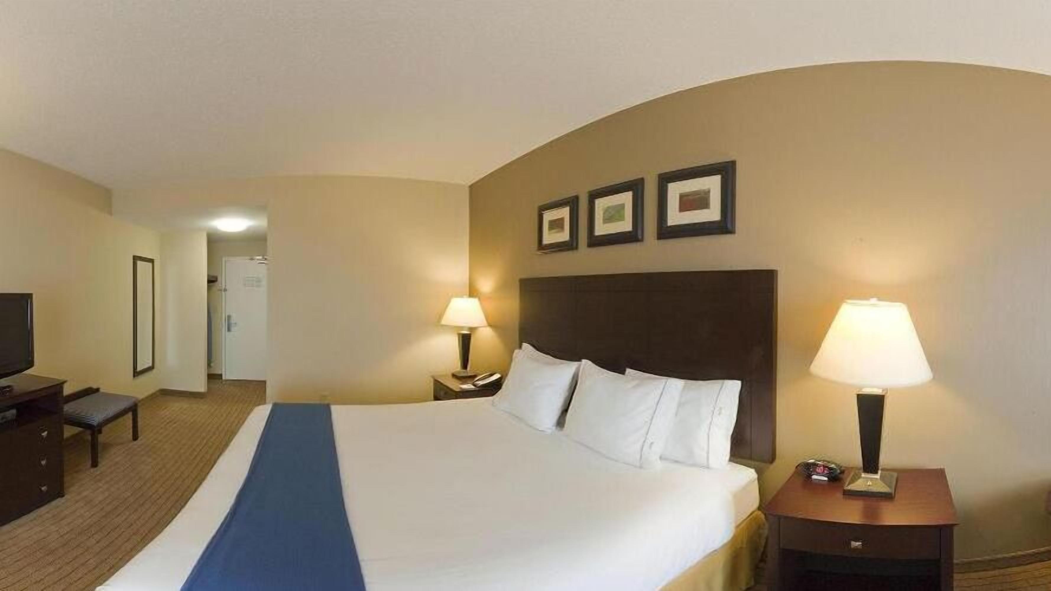 A hotel room with a large bed, two bedside tables with lamps, a TV, and a desk with a chair.