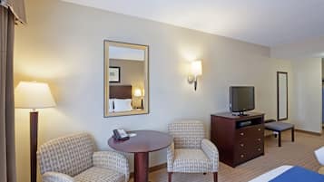 A hotel room with a bed, two patterned chairs, a small table, a TV on a dresser, and a mirror on the wall.