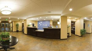 A reception area with a curved desk, a blue wall with a sign, and a tiled floor. - Holiday Inn Express Hotel & Suites Malone by IHG (Malone)