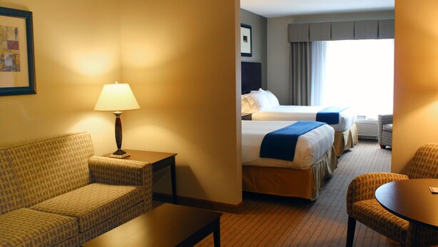 A hotel room with a sofa, a table, a lamp, a bed with two pillows, a chair, and a window. - Holiday Inn Express Hotel & Suites Malone by IHG (Malone)