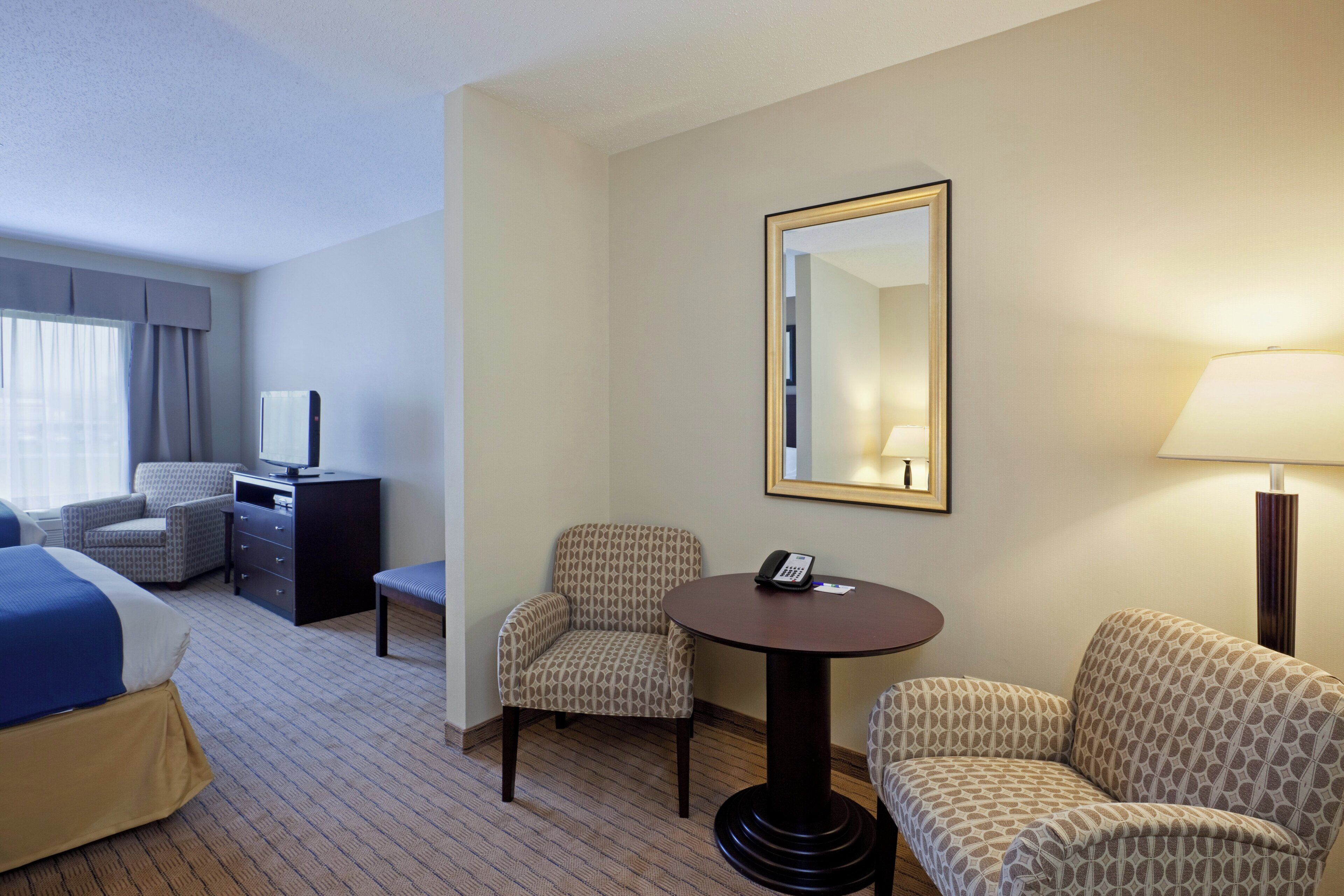 Une chambre d’hôtel comprenant un lit, un bureau avec un ordinateur, deux fauteuils, une petite table avec un téléphone et une lampe.