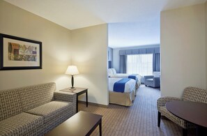 A hotel room with a sofa, a table, a lamp, a bed with a blue blanket, a chair, and a framed picture on the wall. - Holiday Inn Express Hotel & Suites Malone by IHG (Malone)