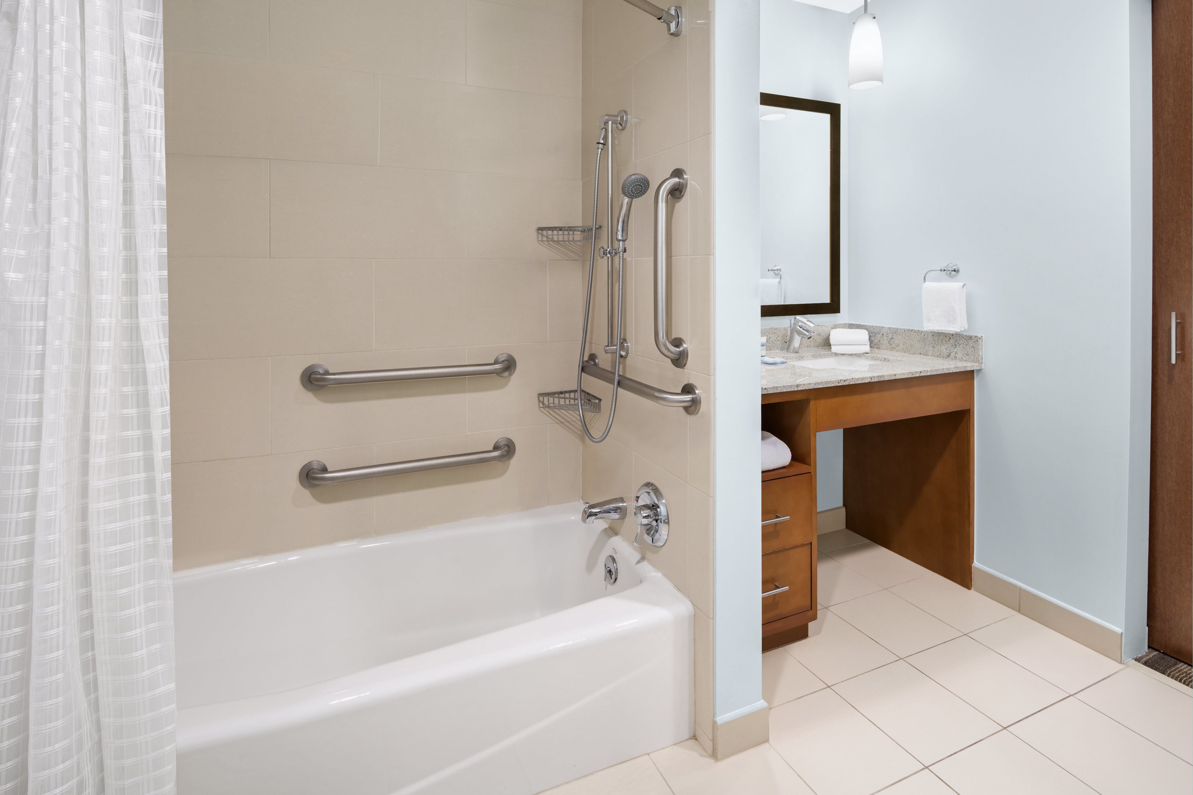 A modern bathroom with a bathtub, grab bars, a shower, a sink, and a mirror.