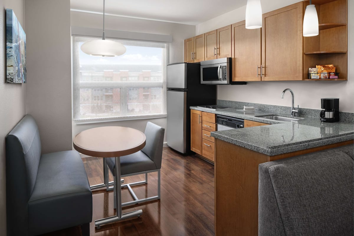 A modern kitchen with wooden cabinets, stainless steel appliances, a granite countertop, and a dining area with a round table and two chairs.