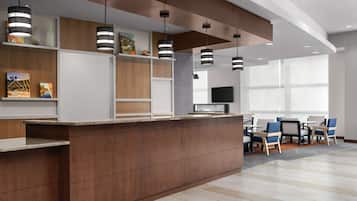 A modern reception area with a wooden reception desk, black pendant lights, and a seating area with blue chairs and a TV.