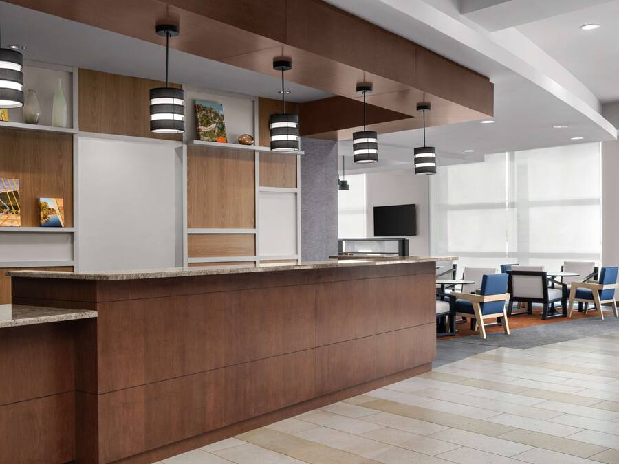 A modern reception area with a wooden reception desk, black pendant lights, and a seating area with blue chairs and a TV.