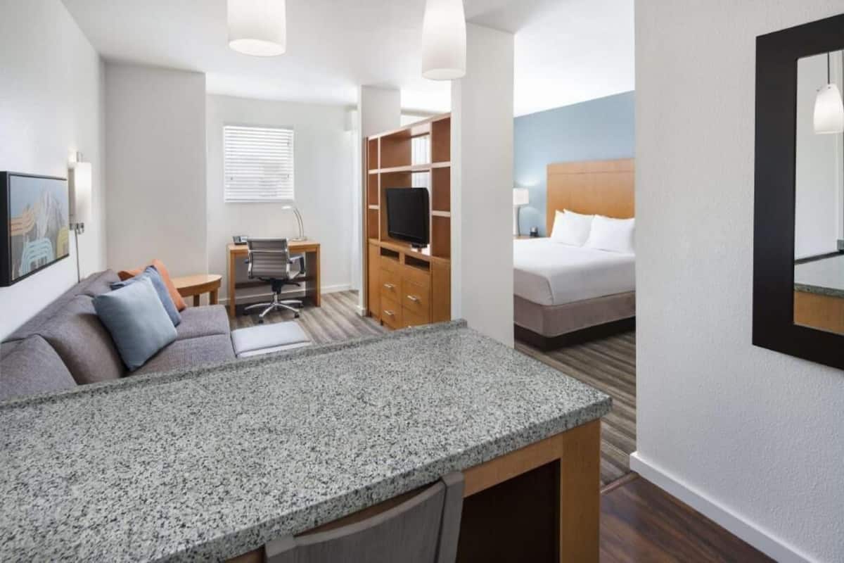A hotel room with a kitchenette, a bed, a TV, and a desk.