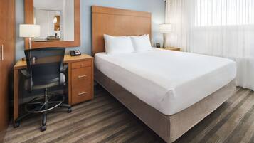 A hotel room with a large bed, a desk with a chair, a mirror, and a nightstand with a lamp.