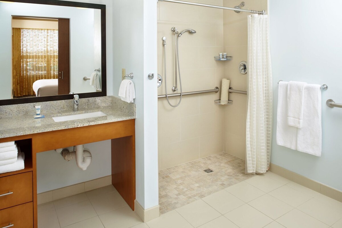 A bathroom with a sink, mirror, shower, and towel rack.