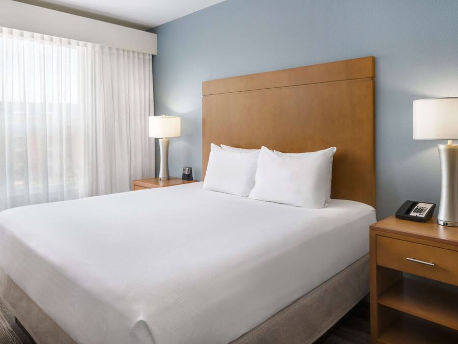 A hotel room with a large bed, two bedside tables, a lamp on each table, and a window with curtains.