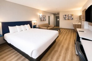 A hotel room with a large bed, a desk, a chair, and artwork on the walls.