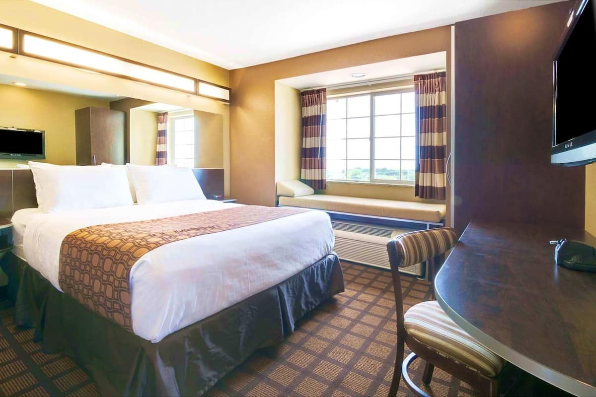 A hotel room with a bed, a desk, a chair, a television, and a window with curtains.