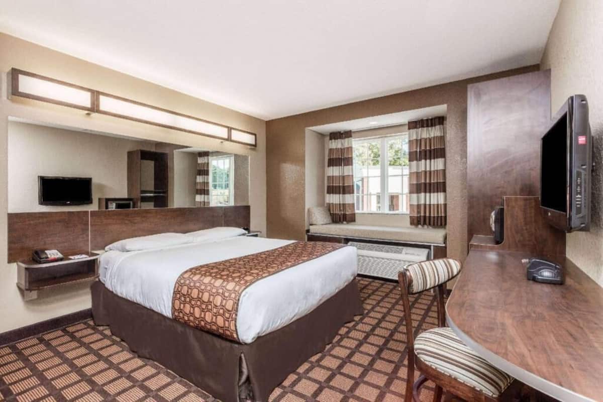 A hotel room with a bed, a desk, a chair, a TV, and a window with curtains.