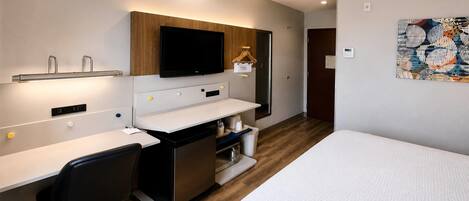 Een moderne hotelkamer met een bed, een bureau, een stoel, een televisie en een badkamer.