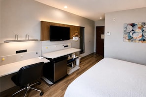 A modern hotel room with a bed, a desk, a chair, a television, and a bathroom.